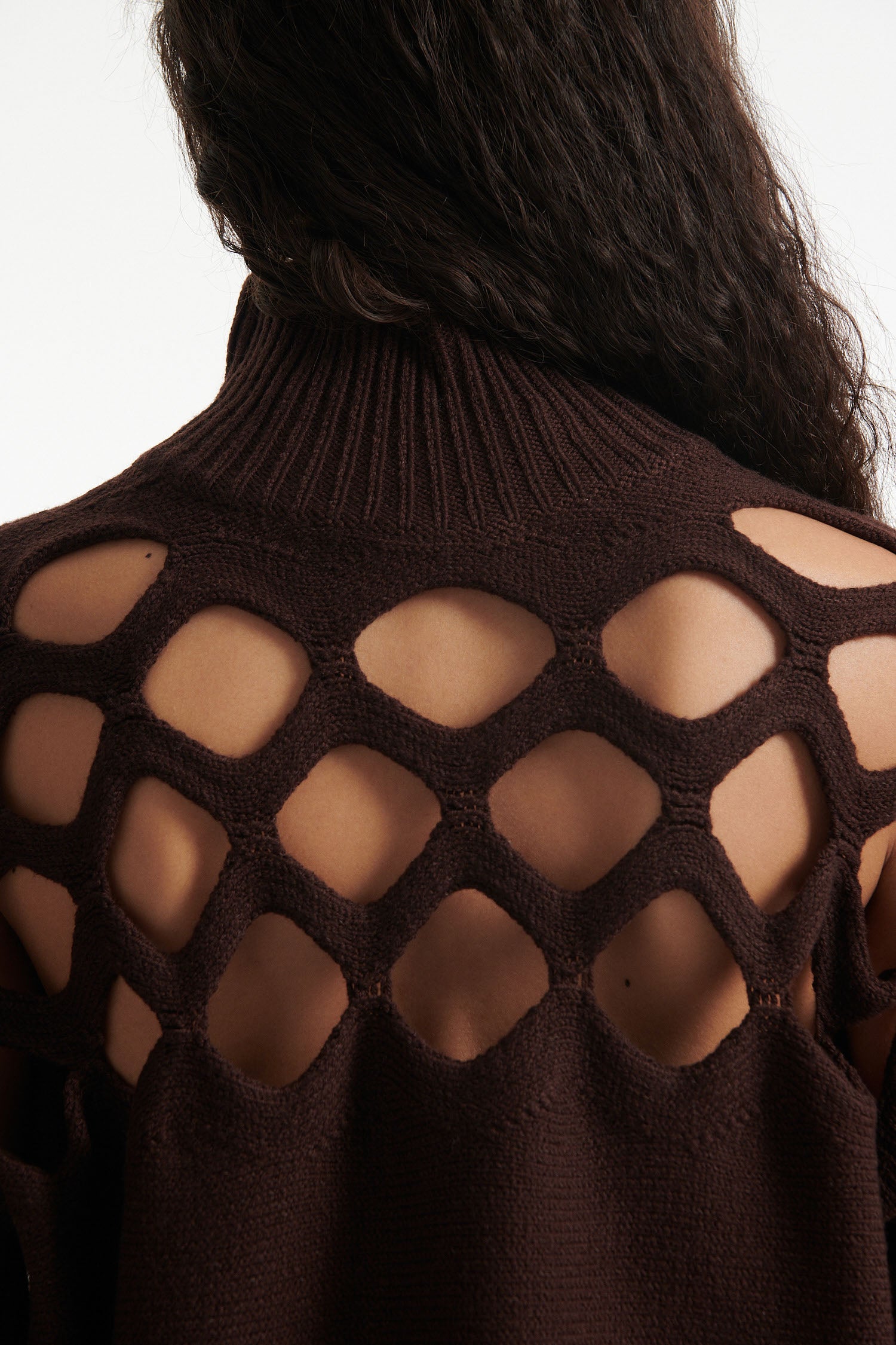 Female model wears open-knit brown long sleeve turtleneck and open-knit brown skirt with black high heels on white background. 