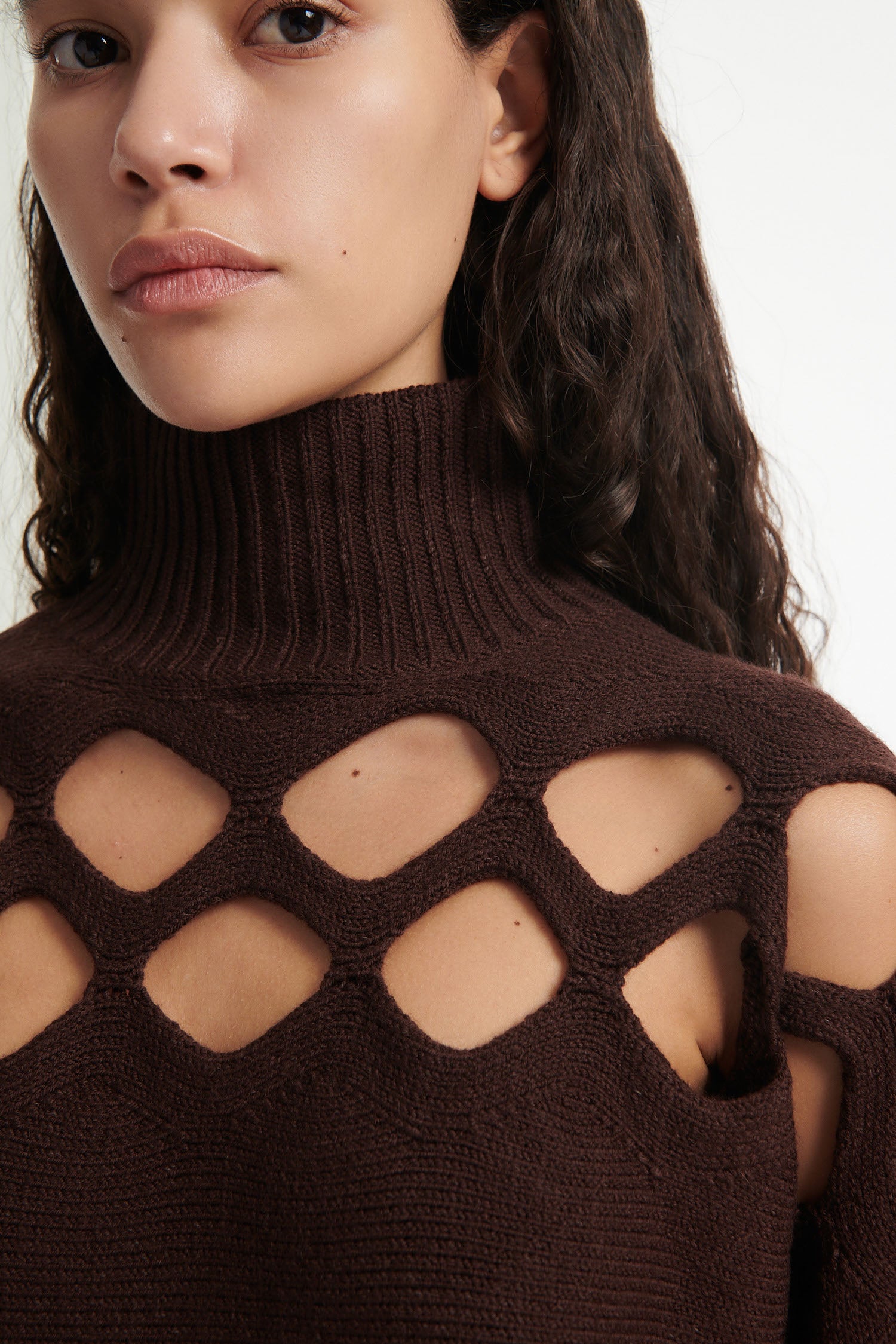 Female model wears open-knit brown long sleeve turtleneck and open-knit brown skirt with black high heels on white background. 