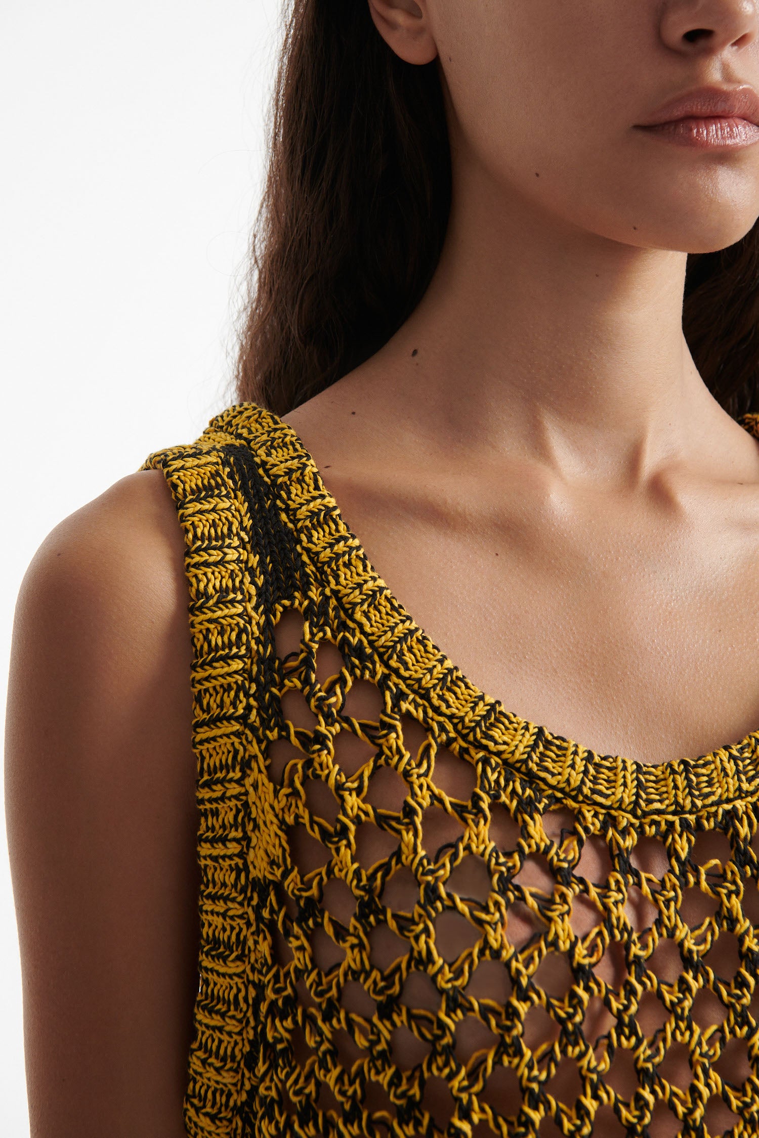 Female model wears yellow mesh tank dress, black high heel boots, and chunky silver bracelet on white background. 