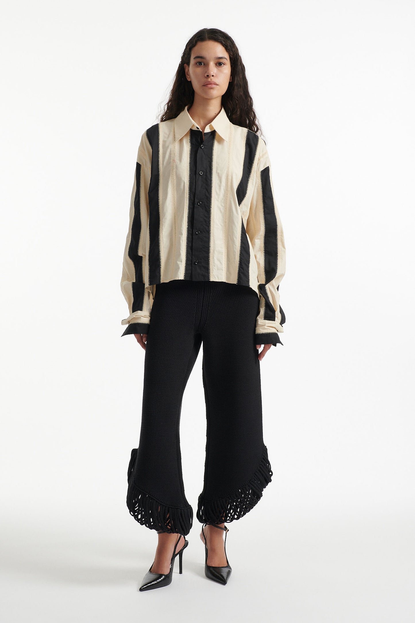 Female model wears off-white and black vertical striped panel button down shirt with cotton black pants and black high heel boots on white background. 