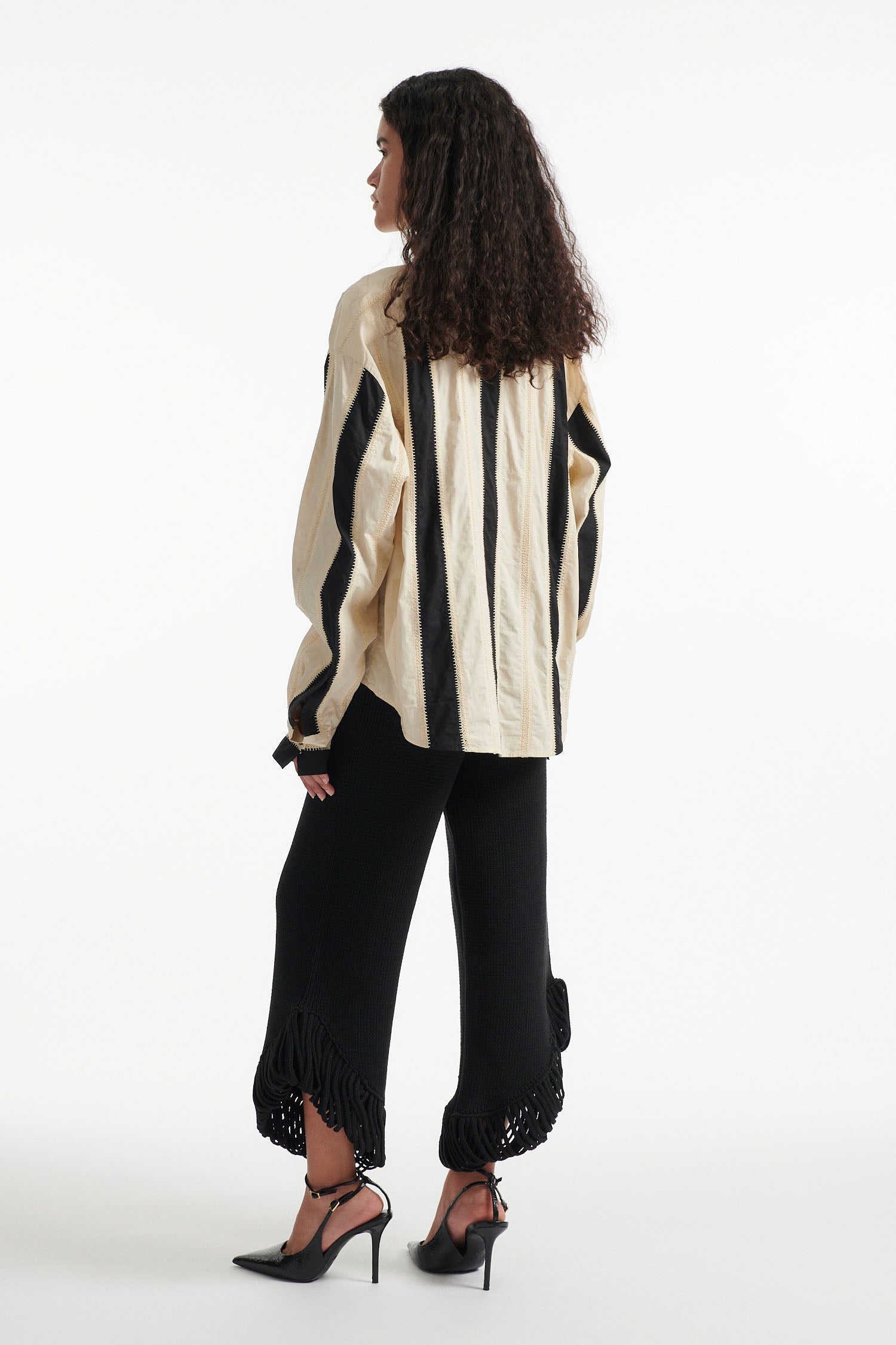 Female model wears off-white and black vertical striped panel button down shirt with cotton black pants and black high heel boots on white background. 