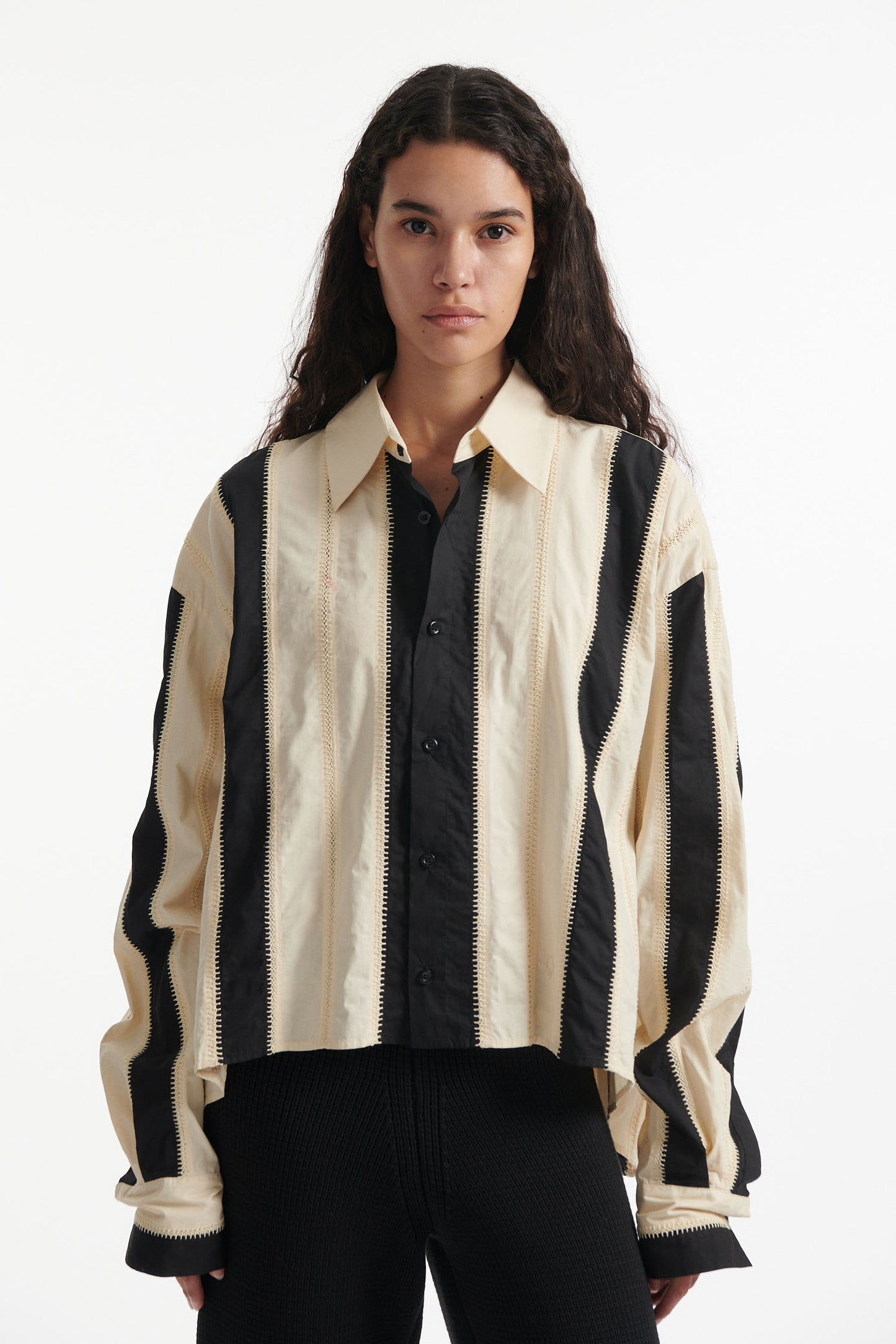 Female model wears off-white and black vertical striped panel button down shirt with cotton black pants and black high heel boots on white background. 