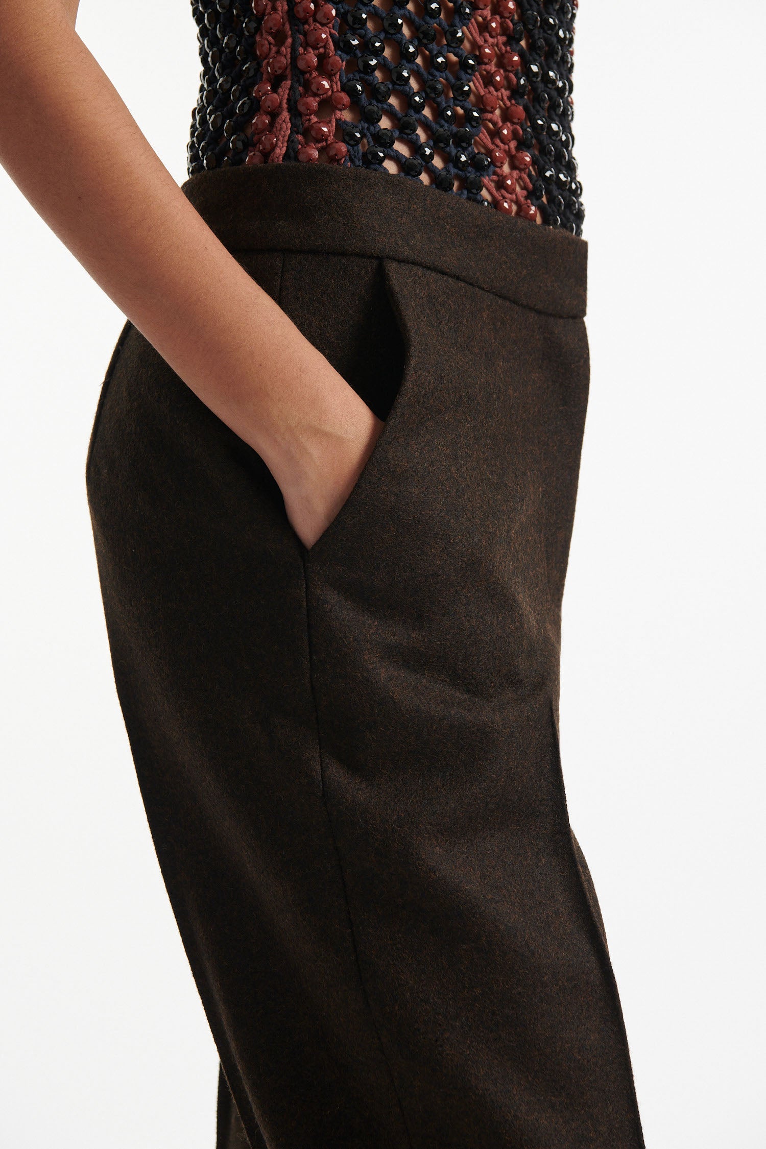 Female model wears striped crystal embellished tank top with slim brown wool trousers and black high heels on white background.