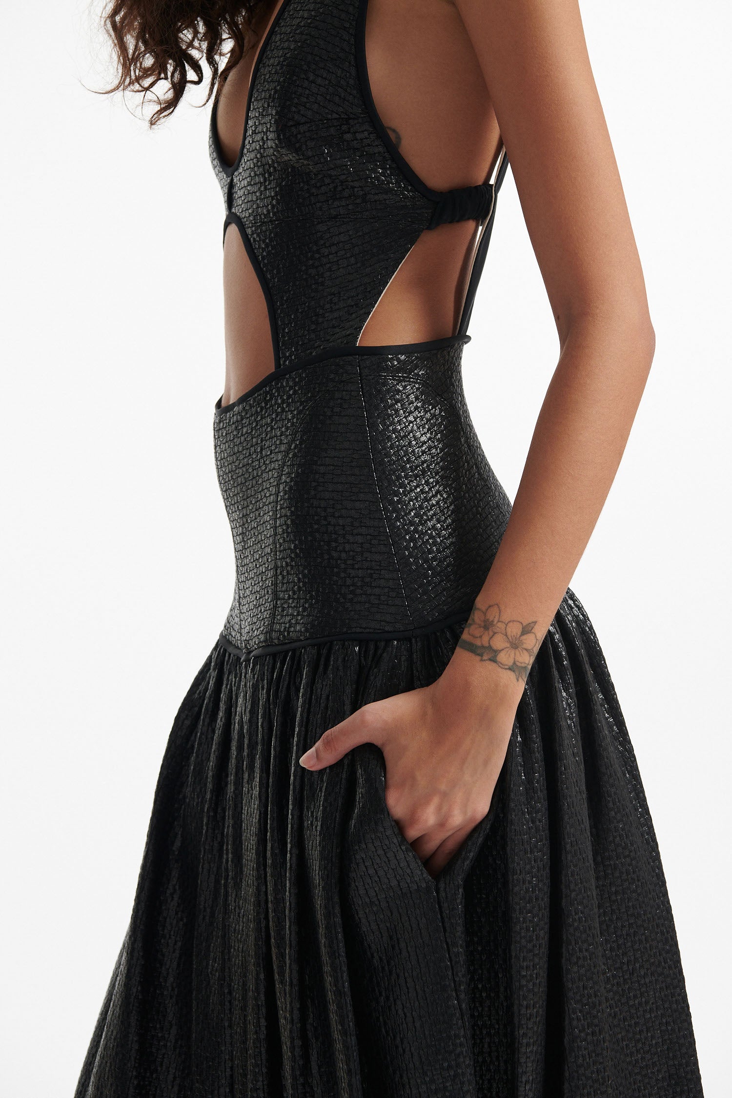 Female model wears open-back black sleeveless dress and black high heels on white background. Dress has cutout in the center.