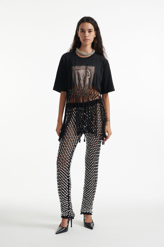 Female model wears deconstructed black graphic tee with crystal embellished tight pants and black high heels on white background. 