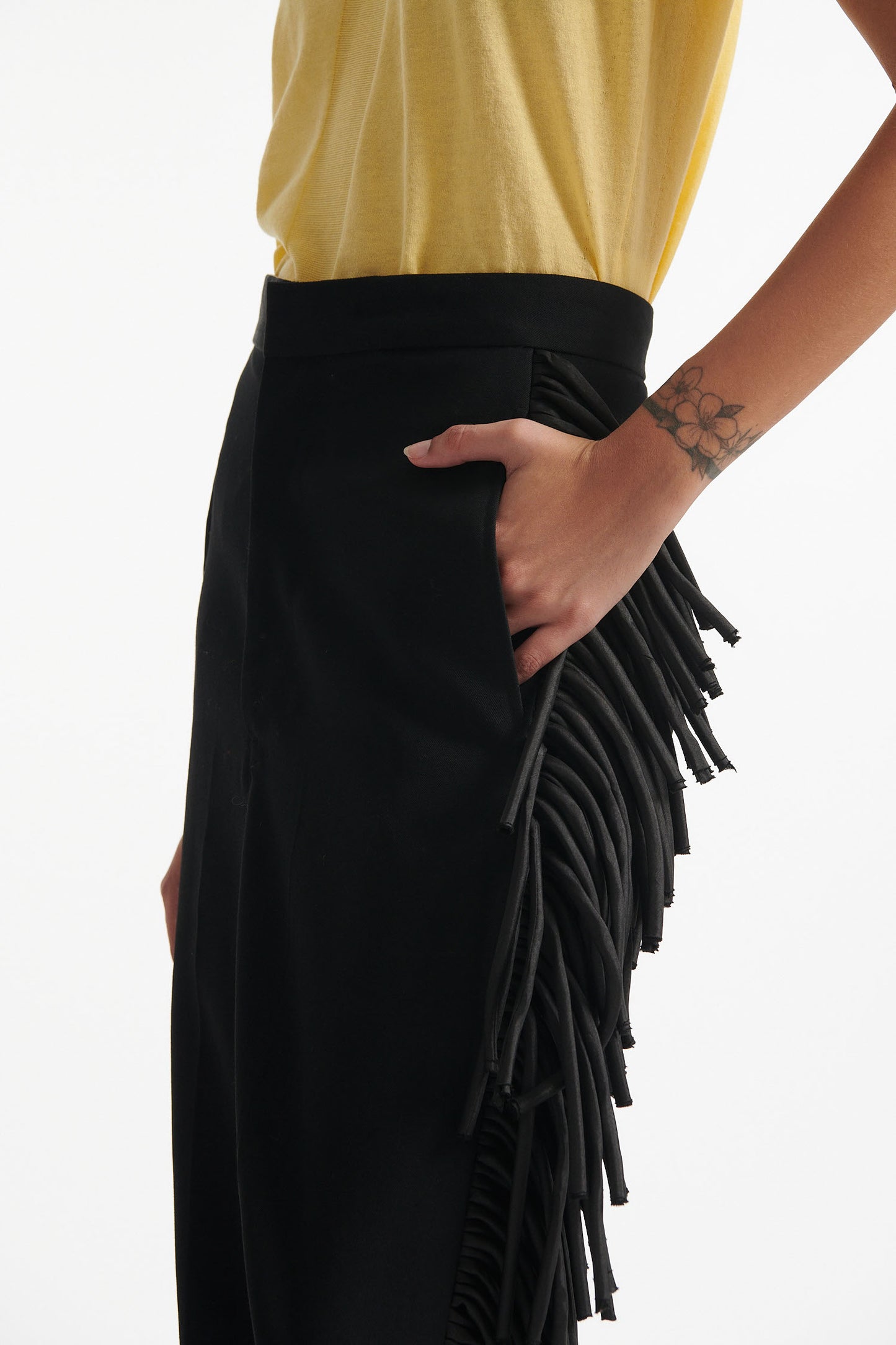 Female model wears long black fringe tuxedo pants with thin yellow cotton shirt and black high heels on white background. 