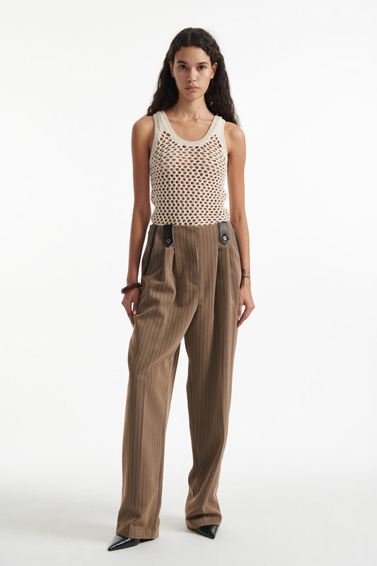 Female model wears beige cotton net tank top with brown pinstripe pleated trousers and black high heels on white background.