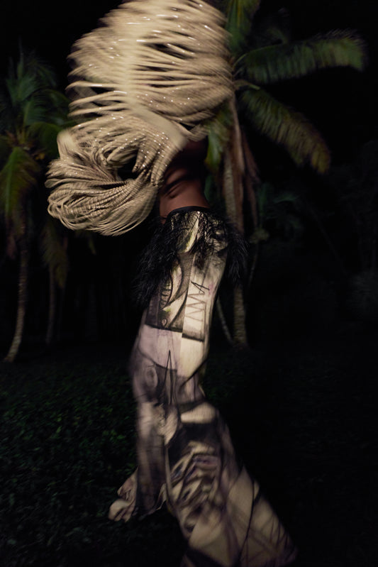 A woman dances outside in the dark wearing a beige fringe bolero and an abstract print long skirt.