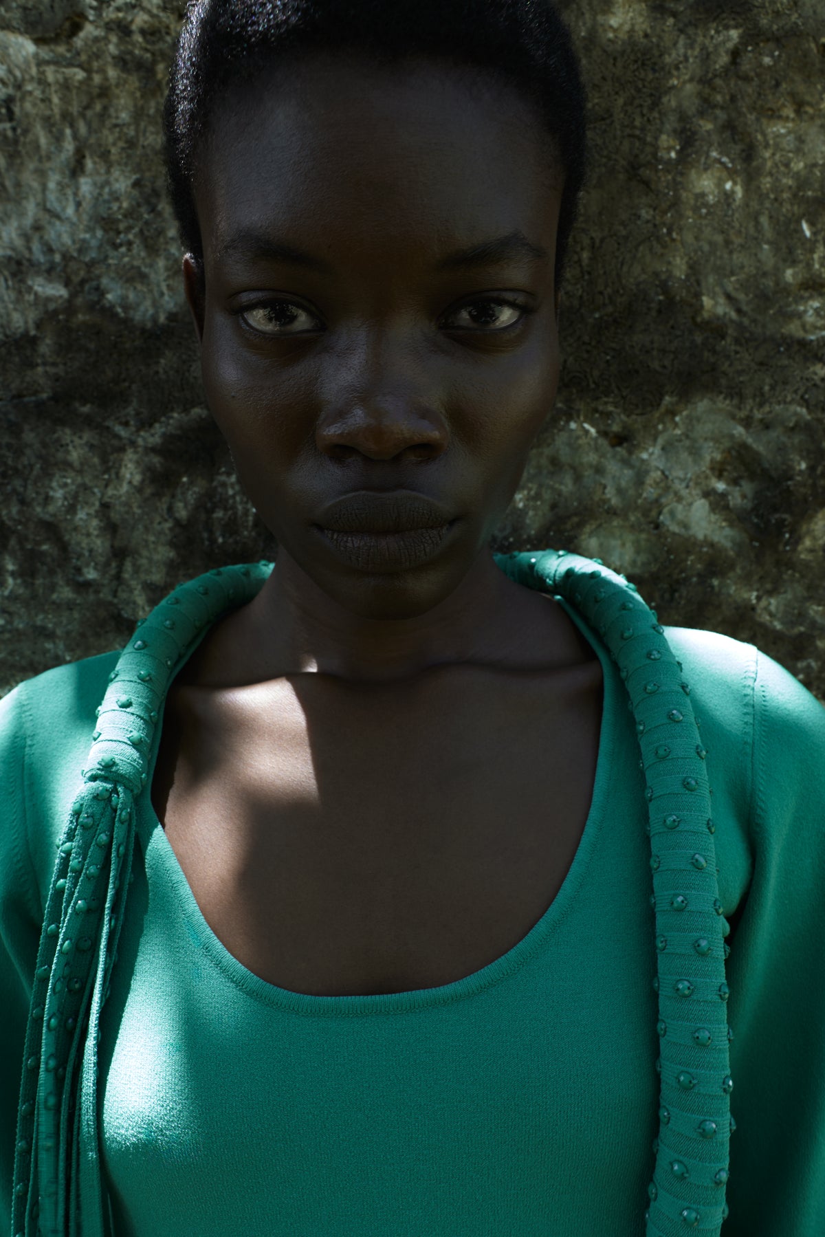 A model stands outdoors in front of a rock wearing a green scoop neck top with embellished fringe.