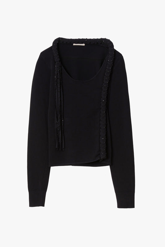 A black long-sleeve knit top with a scoop neckline, featuring a draped front overlay with fringe and beaded trim details, shown against a plain white background.