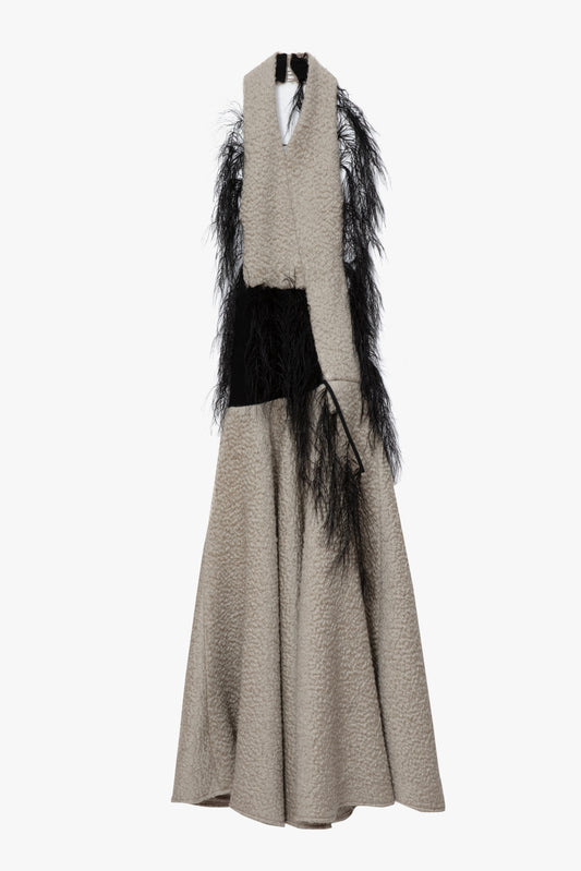A flat image of a textured parchment  halterneck,maxi dress with a wide collar, a black feathered detail. Photographed against a white background.