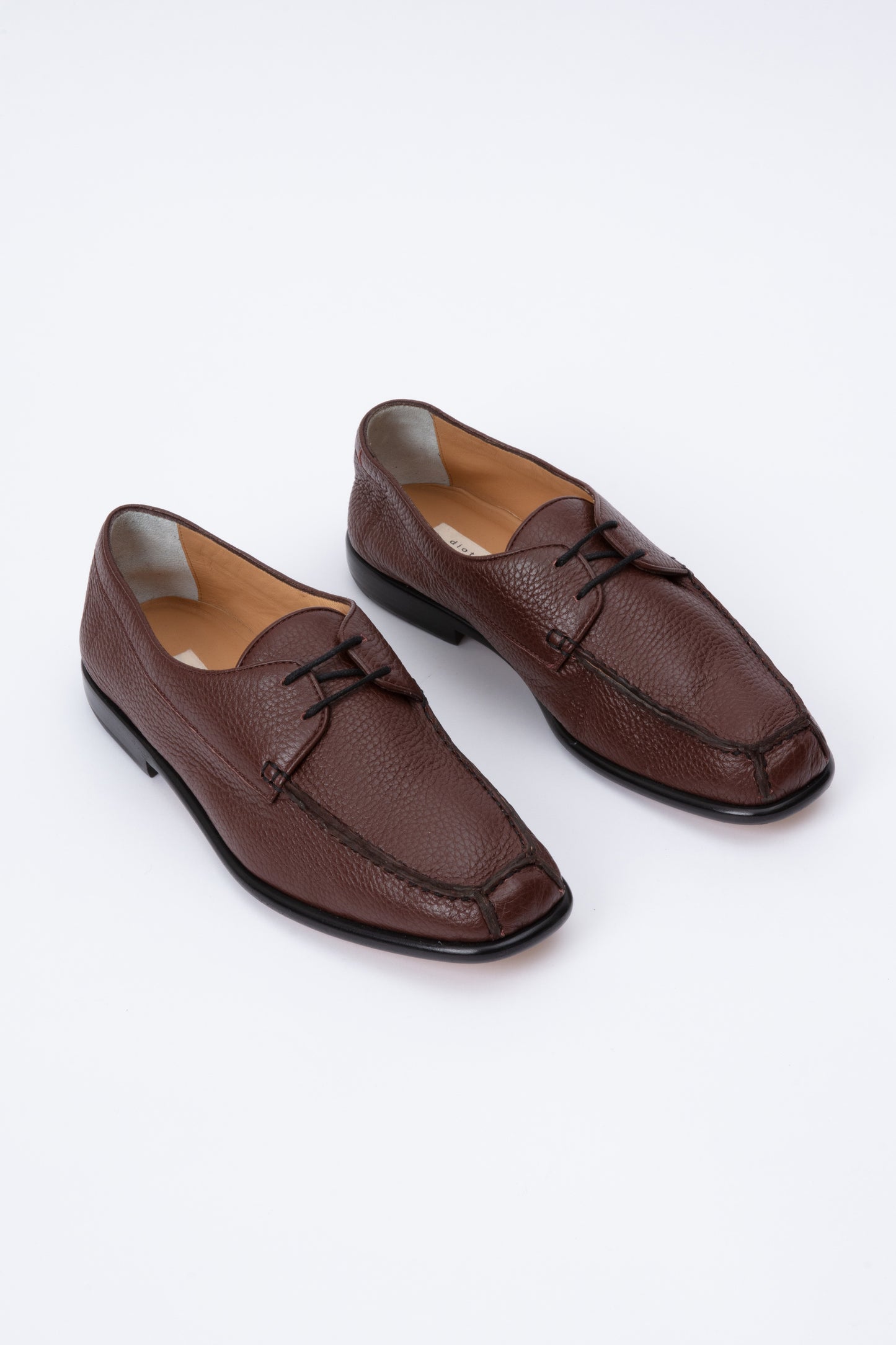 Chocolate brown pebbled leather moccasins with short 1 inch heel and black stitching. Back panel ties at front over short tongue and comes to a squared off point at the toe.