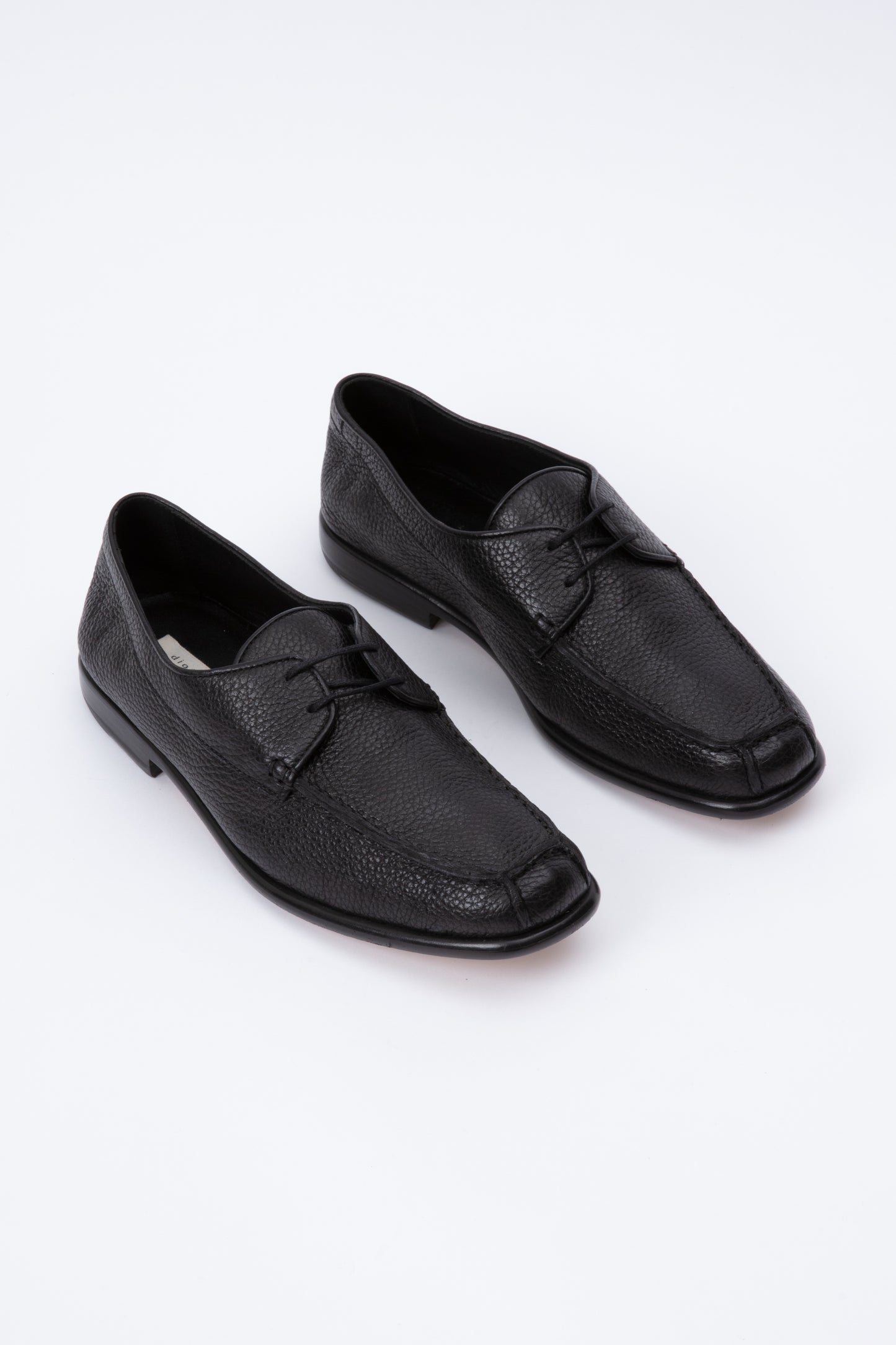 Black pebbled leather moccasins with short 1 inch heel. Back panel ties at front over short tongue and comes to a squared off point at the toe.