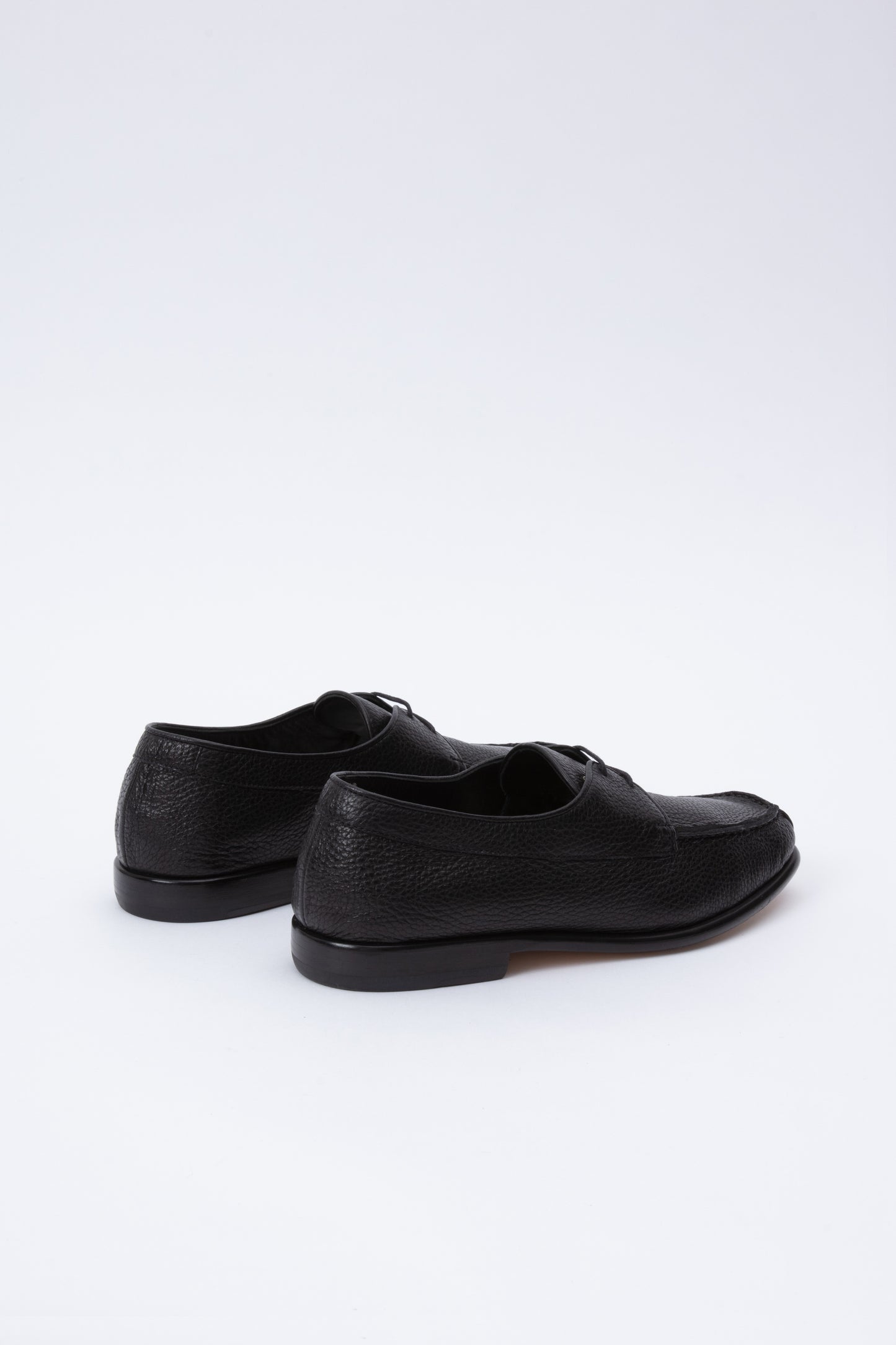 Black pebbled leather moccasins with short 1 inch heel. Back panel ties at front over short tongue and comes to a squared off point at the toe.