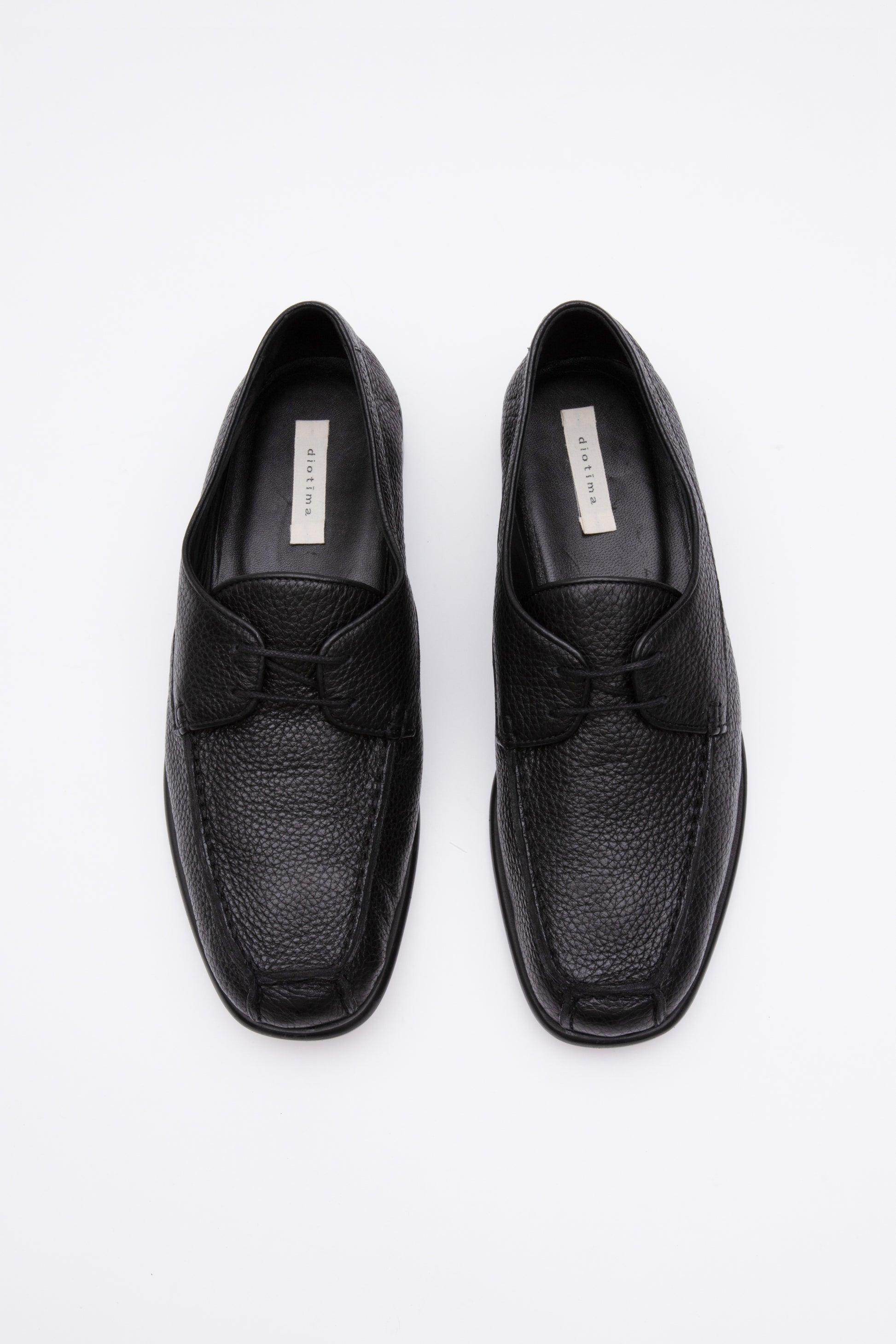 Black pebbled leather moccasins with short 1 inch heel. Back panel ties at front over short tongue and comes to a squared off point at the toe.