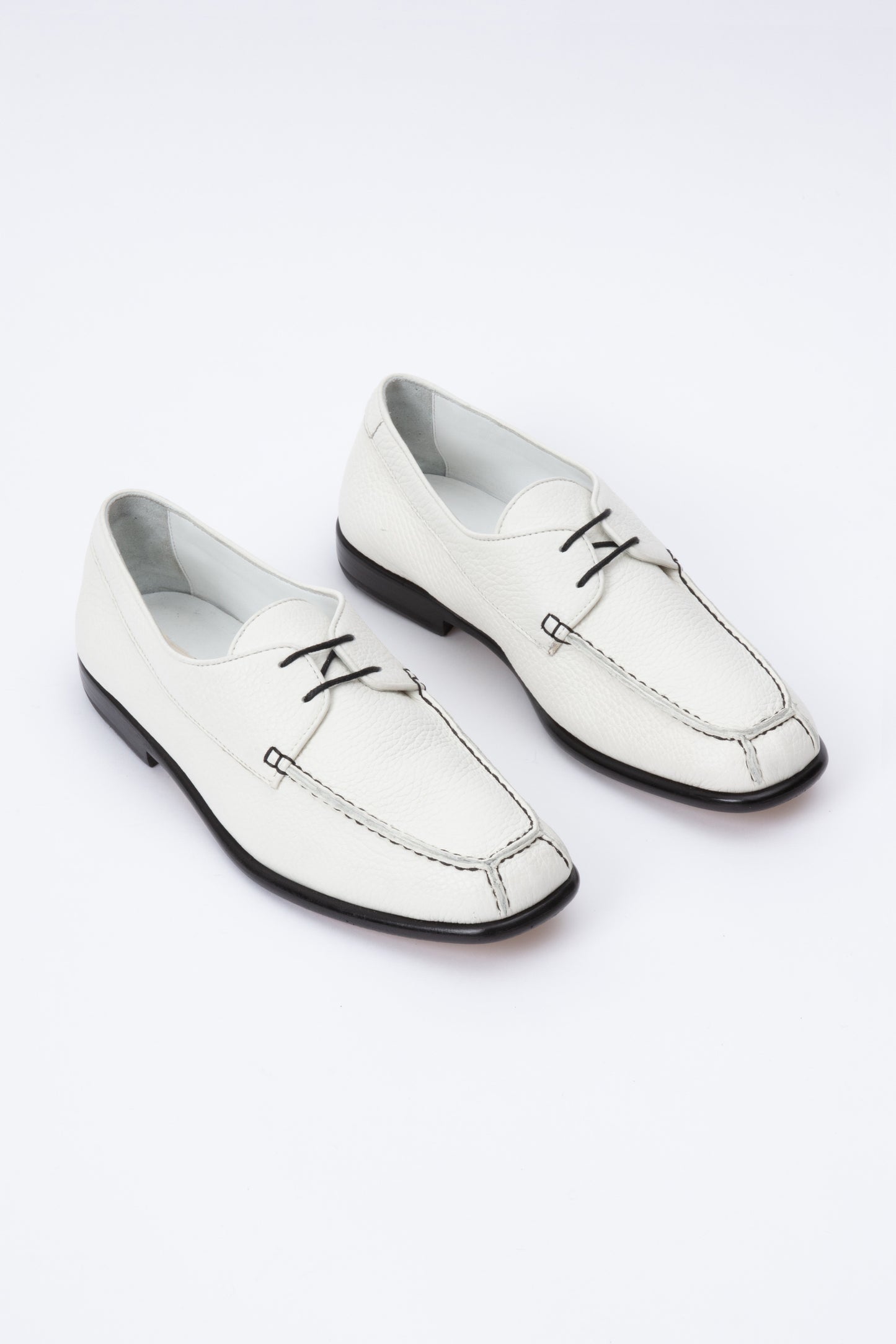 White pebbled leather moccasins with short 1 inch heel and black stitching. Back panel ties at front over short tongue and comes to a squared off point at the toe.