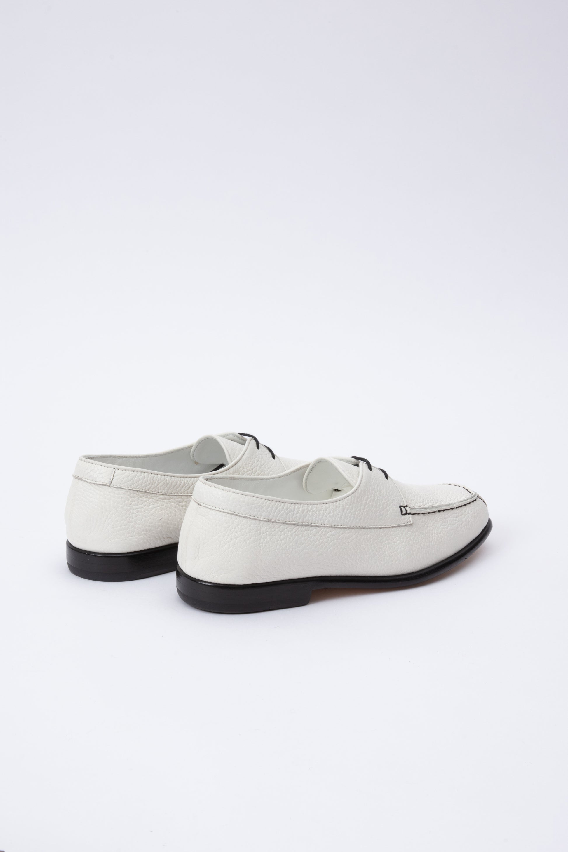 White pebbled leather moccasins with short 1 inch heel and black stitching. Back panel ties at front over short tongue and comes to a squared off point at the toe.