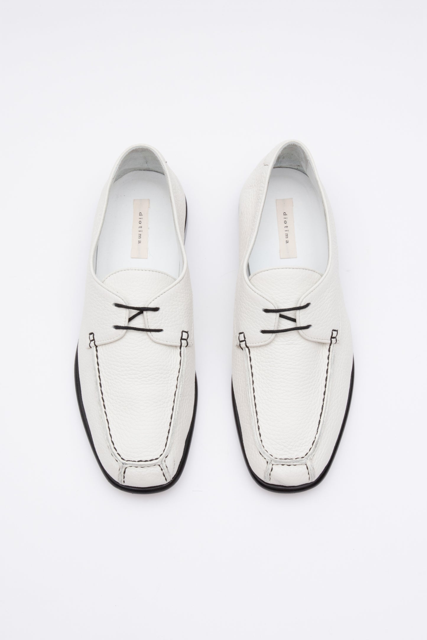 White pebbled leather moccasins with short 1 inch heel and black stitching. Back panel ties at front over short tongue and comes to a squared off point at the toe.