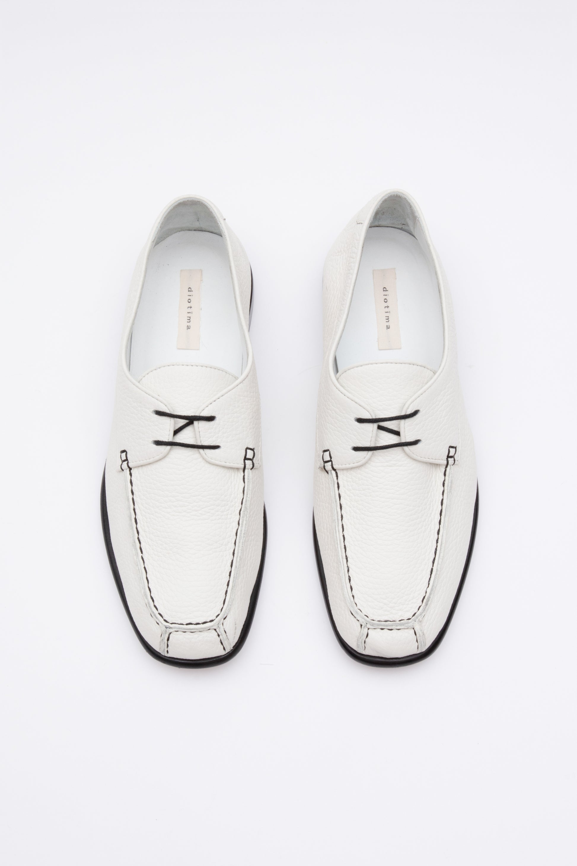 White pebbled leather moccasins with short 1 inch heel and black stitching. Back panel ties at front over short tongue and comes to a squared off point at the toe.