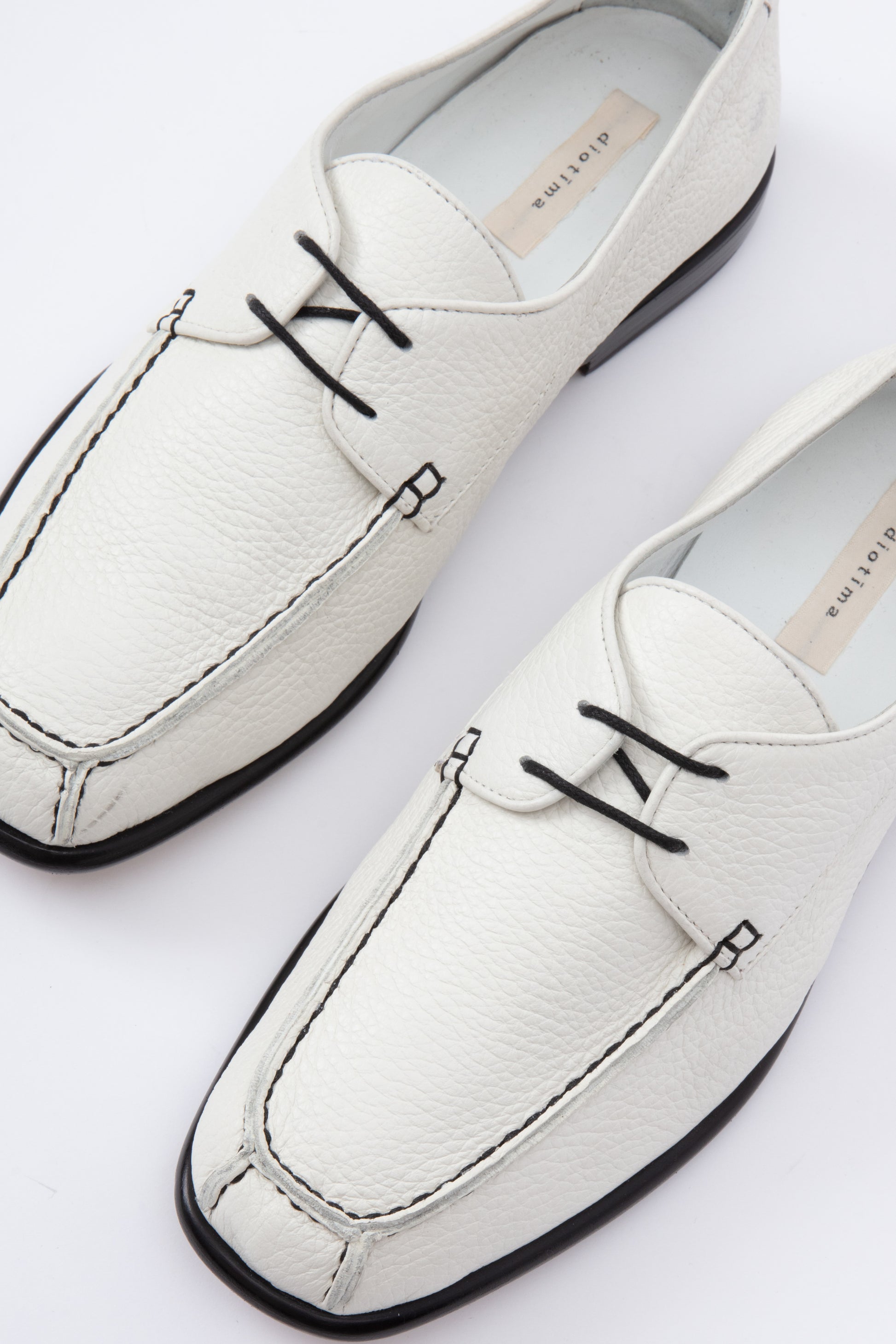 White pebbled leather moccasins with short 1 inch heel and black stitching. Back panel ties at front over short tongue and comes to a squared off point at the toe.