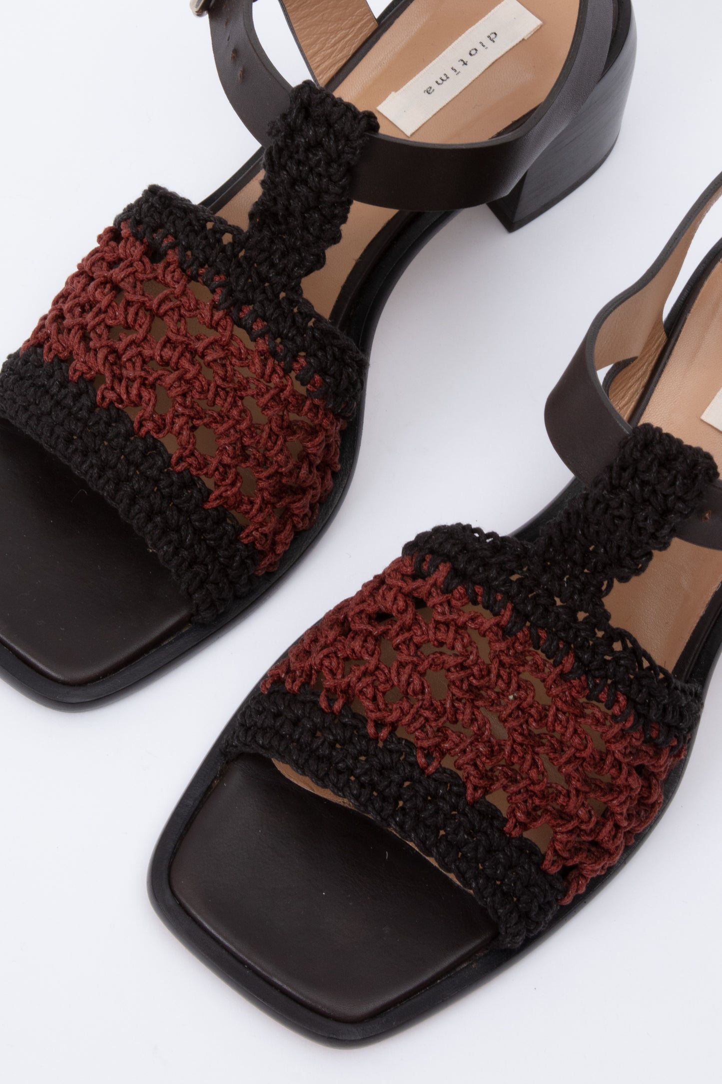 Open toe sandals with black leather base and ankle straps. The block heel is slightly rounded and thick. Connected to the ankle strap is a toe strap made from hand-knit crochet in black and maroon. 