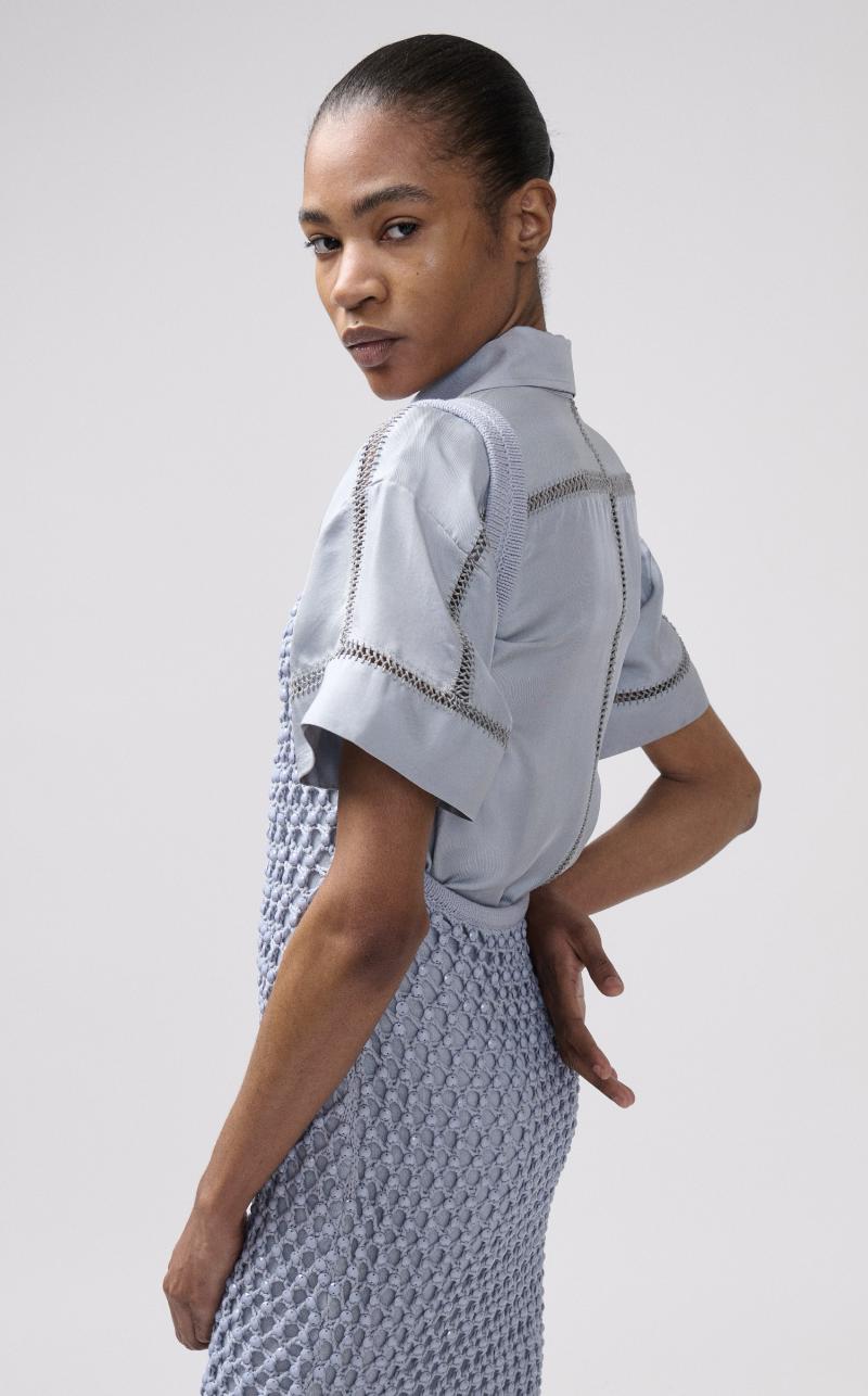 A model wearing a light blue short-sleeve shirt with and a matching textured blue dress.